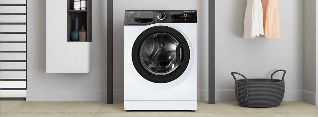 Valge eestlaetav Whirlpool pesumasin kaasaegses vannitoas, kõrval pesukorv ja nagis riided