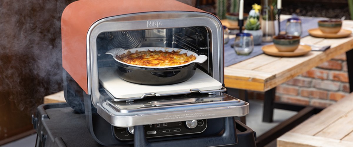 Электрическая печь Ninja Woodfire готовит выпечку на террасе рядом с накрытым столом