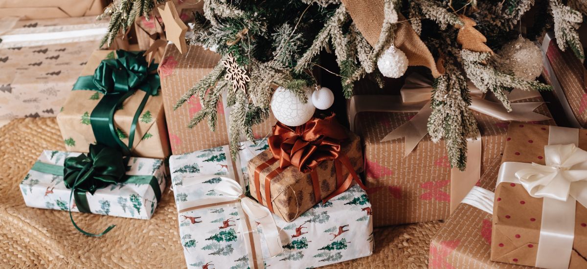 naine istub diivanil kuuse kõrval ja hoiab tassikest, tema kõrval on pakitud jõulukingitus naisele