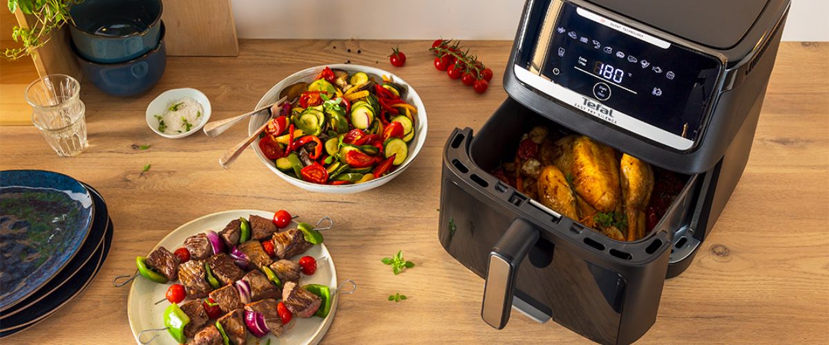 Tefal Easy Fry Silence kuumaõhufritüür küpsetamas tervet kana koos serveerimisvalmis roogadega köögilaual