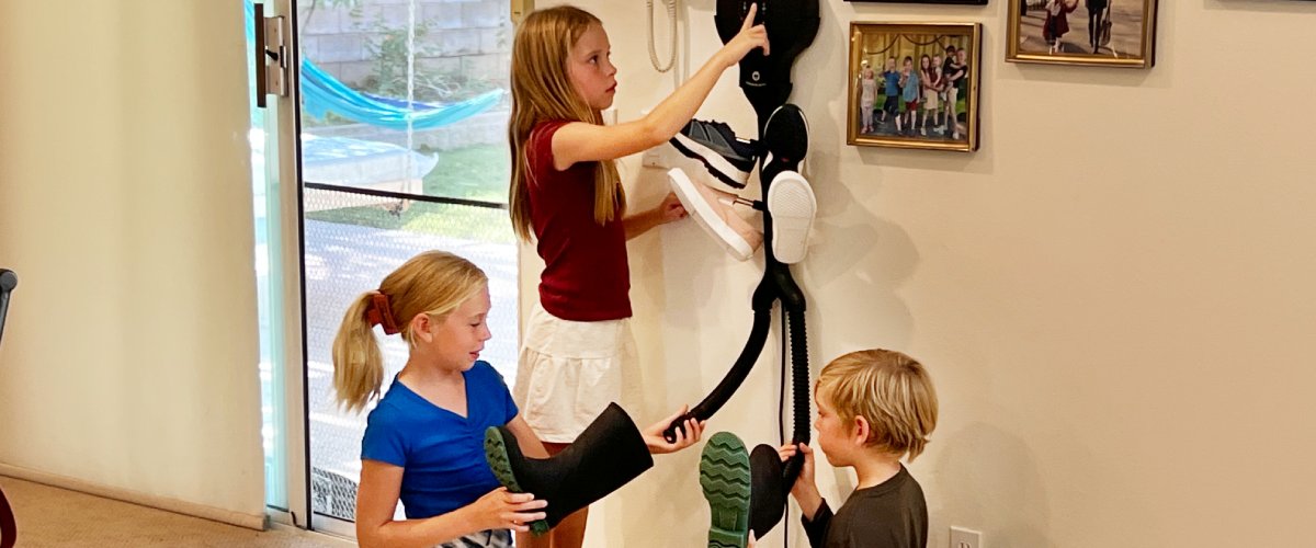 Lapsed kasutavad seinale kinnitatud jalanõude kuivatit esikus, asetades märgi saapad ja jalanõud kuivatamiseks pärast õues käimist.