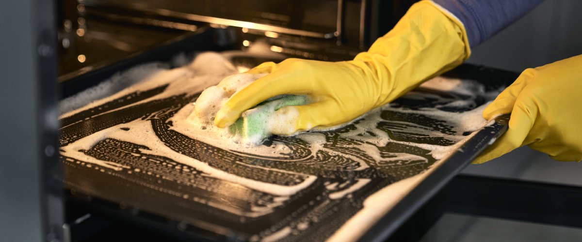 На переднем плане рука чистит духовку губкой и чистящим средством