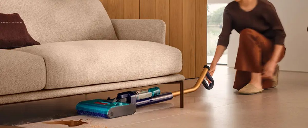 Naine puhastab Dyson WR03 kõvapõrandate puhastajaga diivani alt vedeliku ja mustuse