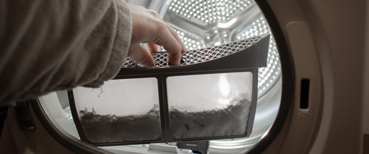 Рука женщины у барабана стиральной машины держит грязный фильтр