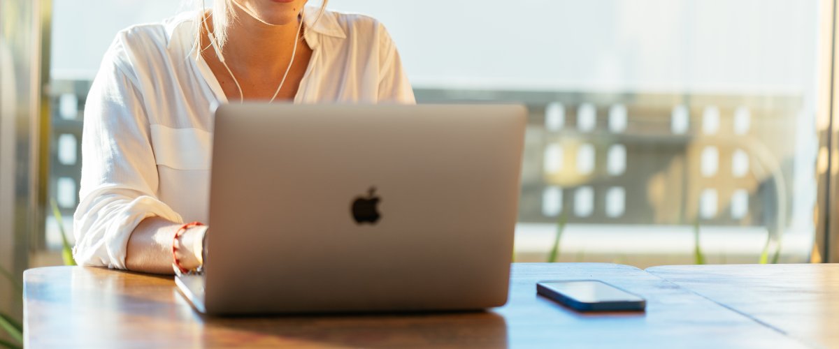 Naeratav naine kasutab MacBooki sülearvutit valgusküllases keskkonnas laua taga