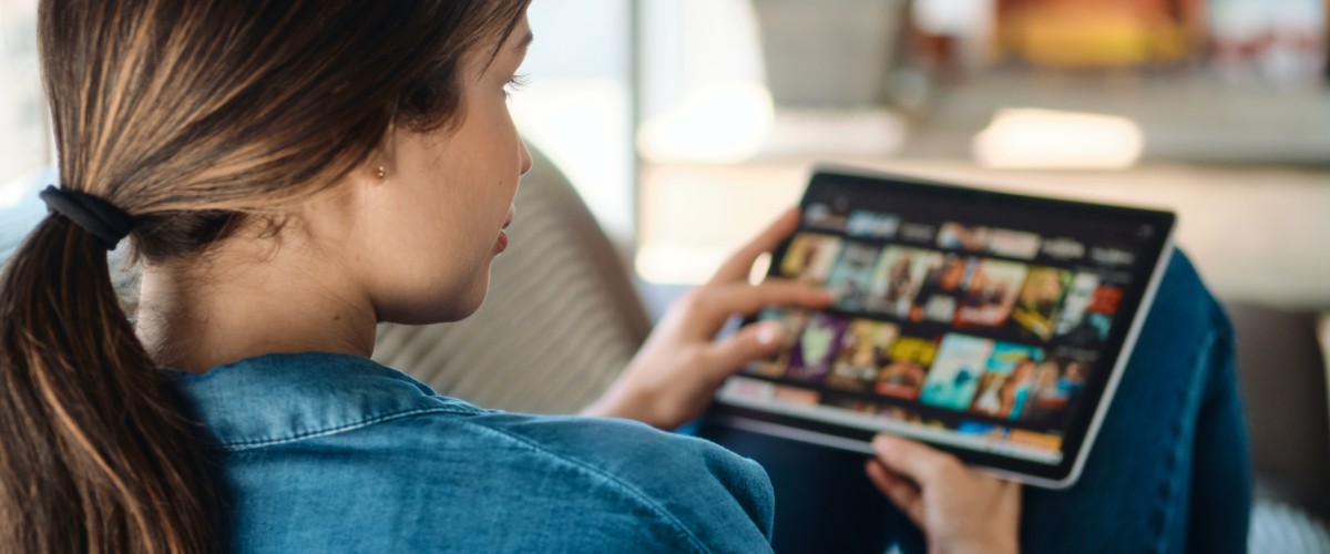 Naine sirvib tahvelarvutis voogedastusteenuse filme ja seriaale kodus diivanil