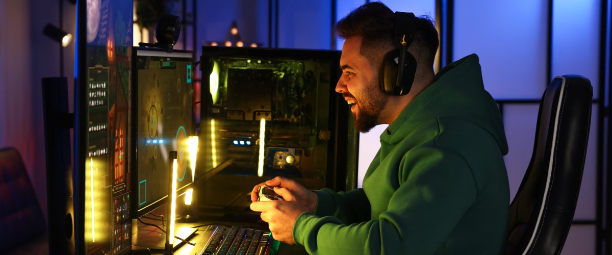 Noor mängur kõrvaklappidega mängib avatud küljega mänguarvutiga kahe monitori taga